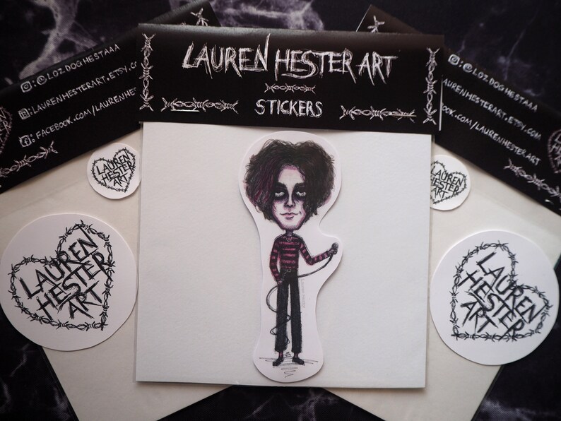 May include: A set of three stickers featuring a cartoon illustration of a person with black hair and a red and black striped shirt holding a microphone. The stickers are on a white background with black barbed wire around the edges. The text "LAUREN HESTER ART" is printed on the stickers.