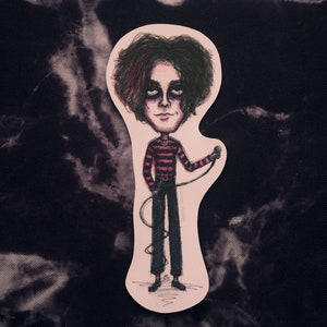 May include: A sticker of a cartoon illustration of a person with dark hair and a red and black striped shirt holding a microphone. The person is standing on a pink background.