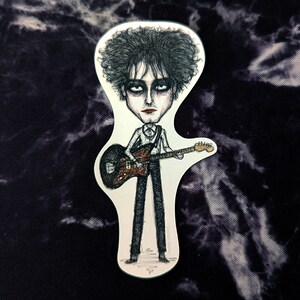 May include: A black and white cartoon illustration of a person with dark hair playing a guitar. The person is wearing a white shirt and black pants. The guitar is brown with a black pickguard.