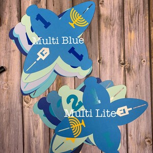 May include: A stack of blue and green paper cut-outs shaped like a star of David. The cut-outs have the numbers 1 and 2, a menorah, and the words "Multi Blue" and "Multi Lite" printed on them.