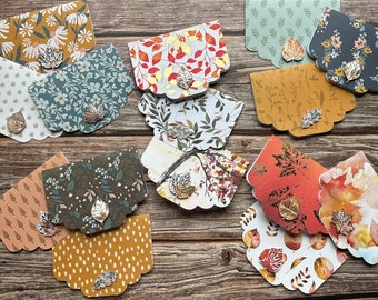 May include: A set of 11 decorative cards with fall-themed designs. Each card features a different pattern of leaves, branches, and floral elements in shades of brown, green, and gold. The cards have a scalloped edge and a small gold leaf embellishment.