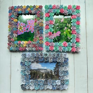 May include: Three picture frames made of paper roses. The frames are in different colors: pink, blue, and white. The frames are all the same size and shape. The frames are all empty.