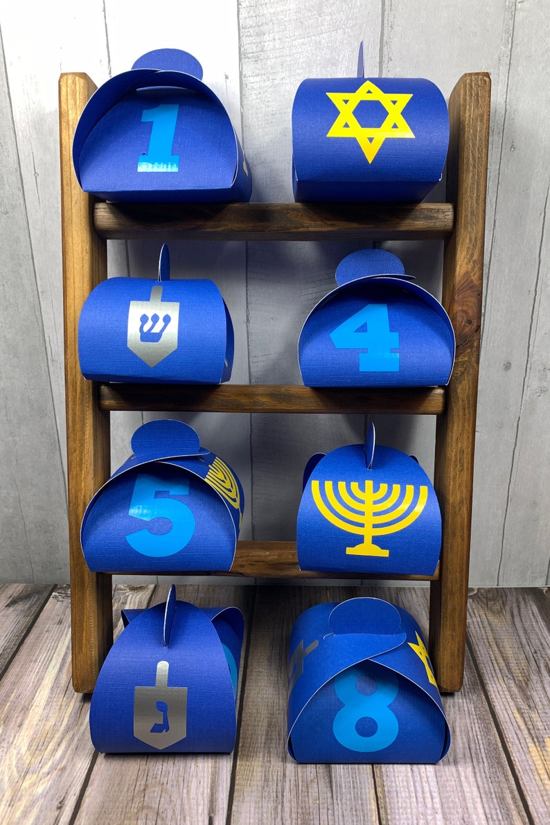 May include: Eight blue gift boxes with different designs for Hanukkah. The boxes are arranged on a wooden shelf. The designs include a Star of David, a menorah, a dreidel, and the numbers 1 through 8.