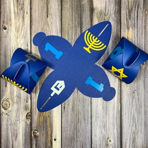 May include: Blue paper gift boxes with yellow and blue designs. The boxes feature symbols associated with Hanukkah, including a menorah, a dreidel, a Star of David, and a Hebrew letter.