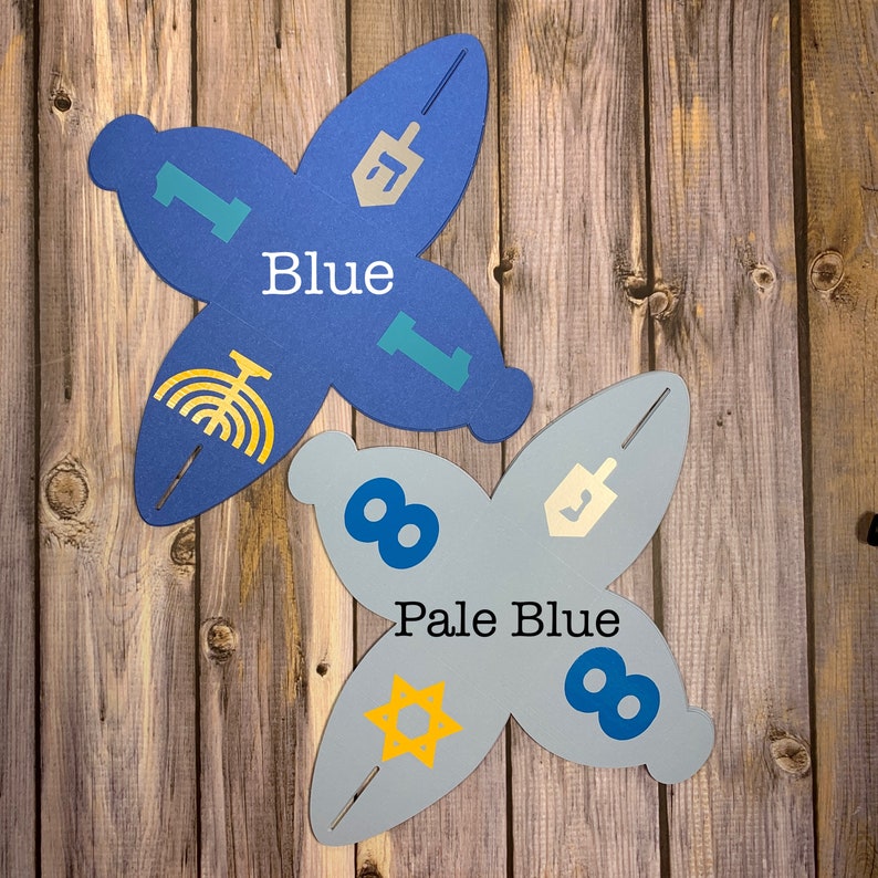 May include: Two blue paper gift boxes shaped like a four-pointed star. The boxes are decorated with Jewish symbols, including a menorah, a Star of David, and a dreidel. The boxes are labeled "Blue" and "Pale Blue".