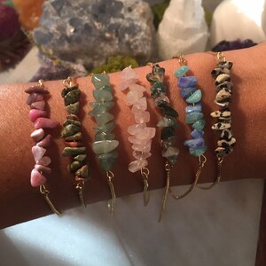 May include: Seven gold chain bracelets with different colored gemstone chips. The bracelets feature pink, green, light green, rose quartz, dark green, blue, and brown and white chips.