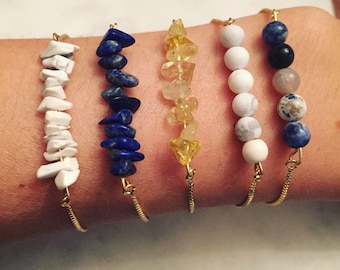 May include: Five gold chain bracelets with different gemstone beads. The bracelets feature white, blue, and yellow beads.
