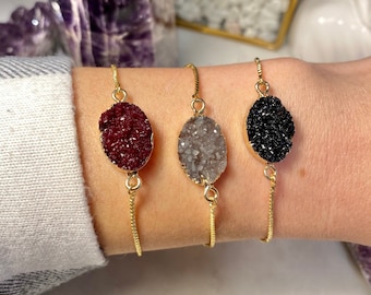 May include: Three gold chain bracelets with oval-shaped crystal charms. The charms are in shades of red, gray, and black.