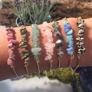 May include: Seven gold chain bracelets with different colored gemstone chips. The bracelets feature pink, green, light pink, green and black, blue, and brown and white gemstone chips.