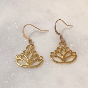 May include: A pair of gold-toned earrings featuring a lotus flower design. The earrings are delicate and have a simple, elegant style.