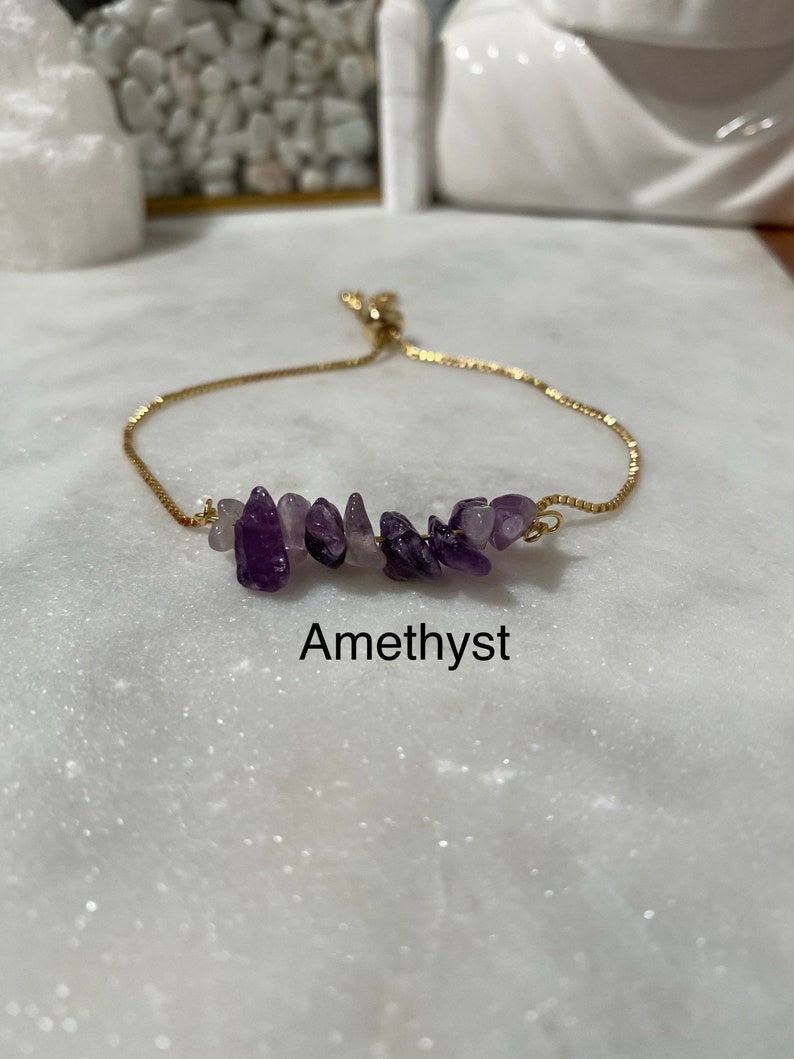 May include: A gold chain bracelet with a cluster of amethyst stones. The bracelet is adjustable and has a sliding knot closure. Amethyst.