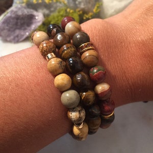 May include: A set of four beaded bracelets with brown, tan, and gold beads. The bracelets are stacked on a person's wrist.