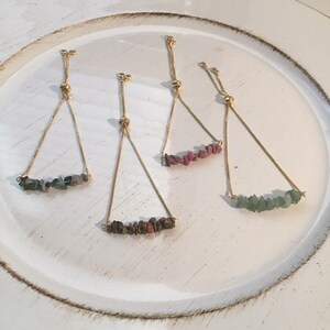 May include: Four adjustable bracelets with gold chains and different colored gemstone beads. The bracelets feature green, pink, and red stones.