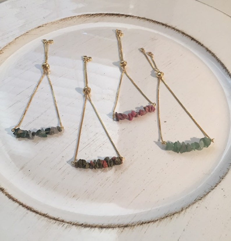 May include: Four adjustable bracelets with gold chains and different colored gemstone beads. The bracelets feature green, pink, and red stones.