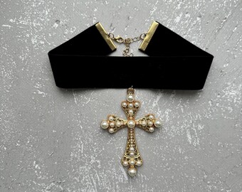 May include: A black velvet choker necklace with a gold cross pendant adorned with white pearls.