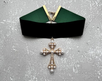May include: A dark green velvet choker necklace with a gold chain and a gold cross pendant adorned with white pearls.
