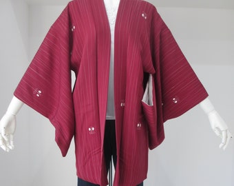 Puede incluir: Una chaqueta estilo kimono burdeos con rayas verticales y detalles bordados en blanco. La chaqueta, de frente abierto, tiene mangas anchas. Se combina con vaqueros de mezclilla azul oscuro. El conjunto se exhibe en un maniquí.