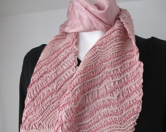May include: A pink satin scarf with a beaded trim and a ruffled edge. The scarf is folded and draped over a black shirt.
