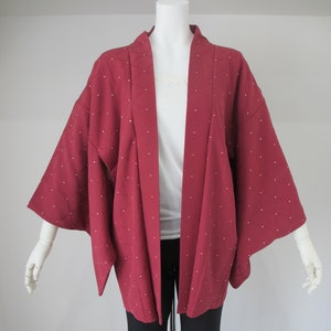 May include: A red kimono with white polka dots. The kimono is worn over a white t-shirt and black pants.