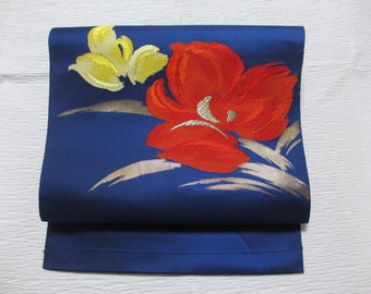 May include: A blue fabric sash with a red and yellow floral design. The sash is folded in half and the floral design is visible on the top half.