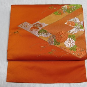 Może przedstawiać: Złożony pomarańczowy materiał z ozdobnym wzorem kwiatów, liści i kształtów geometrycznych w odcieniach pomarańczowego, zielonego i białego.