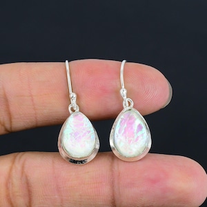 May include: A pair of teardrop-shaped earrings with iridescent white and pink stones set in silver. The earrings have a simple hook design and are displayed against a dark background.
