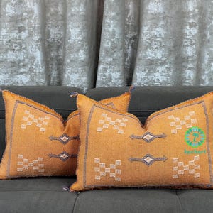 May include: Two decorative throw pillows with a geometric pattern in shades of brown, white, and beige. The pillows are made of a soft, textured fabric and have a subtle sheen.