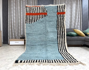 May include: A blue and white striped rug with a geometric pattern. The rug has a fringe border and is made of wool.