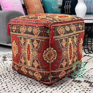 Puede incluir: Un puf cuadrado con borlas, hecho de tejido tejido con un diseño geométrico en rojo, naranja y amarillo.