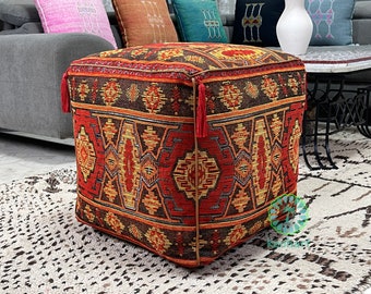 May include: A square ottoman with tassels, featuring a red, orange and yellow patterned woven fabric with a geometric design.