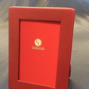 May include: A red leather picture frame with a gold embossed logo that reads "Kitney & Co."