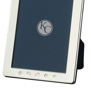 May include: A silver picture frame with a dark blue mount and a silver hallmark on the front. The frame has a stand on the back and is decorated with five small silver circles on the bottom edge.