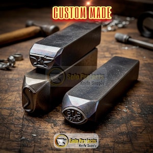 May include: Three rectangular metal stamping tools with dark, oxidized finishes. The tools feature engraved designs on their ends, including an anvil icon and the text 'SJS KNIVES'. The text 'CUSTOM MADE' appears at the top of the image.