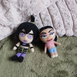 Pode incluir: Duas bonecas de lã feltrada. A boneca da esquerda tem cabelo preto, olhos roxos, top preto e calças roxas. A boneca da direita tem cabelo preto, sombra roxa, top rosa e calças azuis, todas feitas com a técnica de feltragem com agulha.