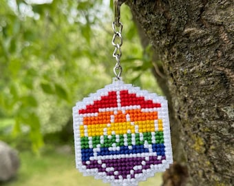 May include: A handmade keychain featuring a colorful rainbow design. The keychain is a small, geometric shape with a white border and a rainbow pattern in red, orange, yellow, green, blue, and purple. It hangs from a silver chain.