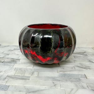 May include: A glossy, round ceramic bowl with a black exterior and red interior. The black surface has a marbled effect with red streaks. The bowl has a wide opening and a pumpkin-like shape. A decorative piece for the home.