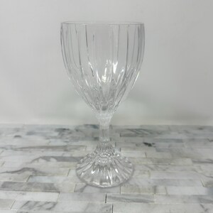 May include: A clear, stemmed wine glass with vertical ribbed detailing on the bowl. The glass has a decorative base and a slender stem. The glass is made of clear glass and is suitable for serving wine or other beverages.