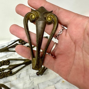 May include: Set of five antique gold-toned metal furniture feet with ornate scrollwork designs. Each foot has a pointed tip and a decorative top.