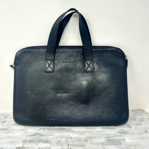 May include: Black leather laptop bag with a top handle and a zipper closure. The bag has a subtle embossed logo that reads "Colefax".