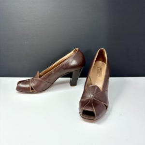 May include: A pair of vintage brown leather peep-toe heels. The shoes have a high heel and a cutout design on the vamp. The heels are dark brown, and the shoes appear to be in good condition.