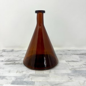 May include: A brown glass vase with a conical shape and a narrow neck. The vase has a smooth, glossy surface and a dark amber color. The vase is likely used for decorative purposes or to hold flowers.