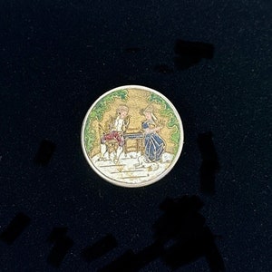 May include: A round, silver-toned button with a colorful enamel design. The design depicts two figures sitting at a table in a garden setting. The figures are wearing colorful clothing and the background is green and gold.