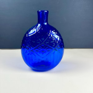 May include: A cobalt blue glass vase with a spherical body and a narrow neck. The surface features a pressed diamond pattern with embossed floral motifs within each diamond shape, creating a textured appearance across the rounded glass vessel.
