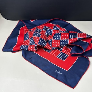 May include: A square scarf featuring a checkered pattern of red and navy blue squares with white polka dots. The scarf has a wide navy blue border with a thin red edge and the word Echo printed in white script in the lower right corner.