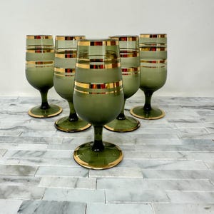 May include: Set of six green glass wine glasses with gold stripes. The glasses have a frosted finish and are perfect for serving wine or cocktails.