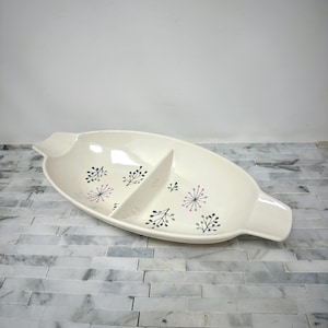 May include: Cream-colored, divided serving dish with a mid-century modern design. The oval dish features a central divider and is decorated with stylized floral patterns in black, gray, and pink. It has handles on each end.