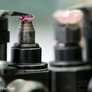 Może przedstawiać: Zbliżenie na r&oacute;żowy kamień szlachetny trzymany w metalowej klamrze. Kamień jest polerowany i kształtowany przez maszynę.