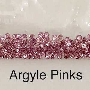 Może przedstawiać: Zbliżenie na kolekcję małych, r&oacute;żowych diament&oacute;w Argyle. Diamenty są luźne i rozrzucone na białym tle. Pod diamentami widnieje napis "Argyle Pinks".