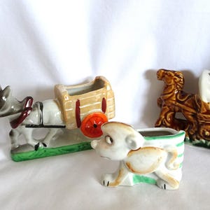 May include: Three ceramic planter figurines. A donkey pulling a wagon, a dog, and a horse pulling a covered wagon. The figurines are all in shades of brown, white, and green.
