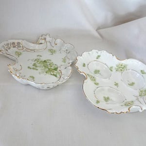 May include: Two antique porcelain serving dishes. One is a scalloped shape with a pierced design, the other is leaf-shaped with three oval indentations. Both have gold trim and a floral pattern in green.